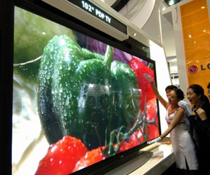Delicate Korean booth babes too tiny to measure the full girth of the LG 102-inch plasma screen.